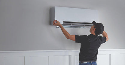 Technician installing a wall-mounted air conditioner inside a home.