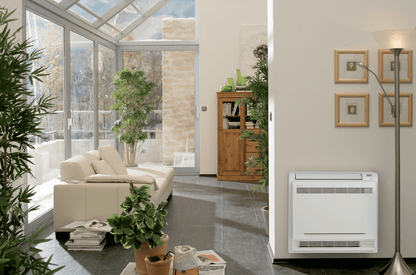 Floor-mounted air conditioning unit installed in a modern living room with large windows and indoor plants.