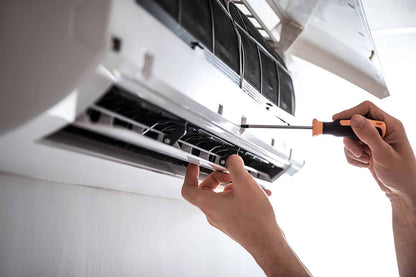 Technician performing air conditioning maintenance by using a screwdriver to inspect and service an air conditioning unit.