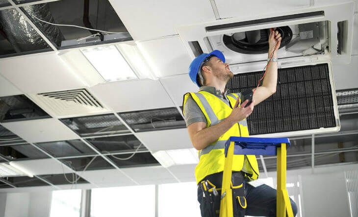 Experienced technician performing air conditioning maintenance and inspection in a commercial building ceiling system.