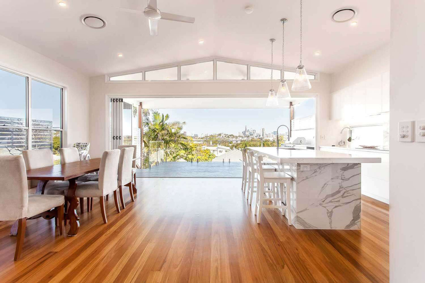 Modern open-plan living room with ducted air conditioning and wooden flooring, featuring a dining area, kitchen island, and large windows.