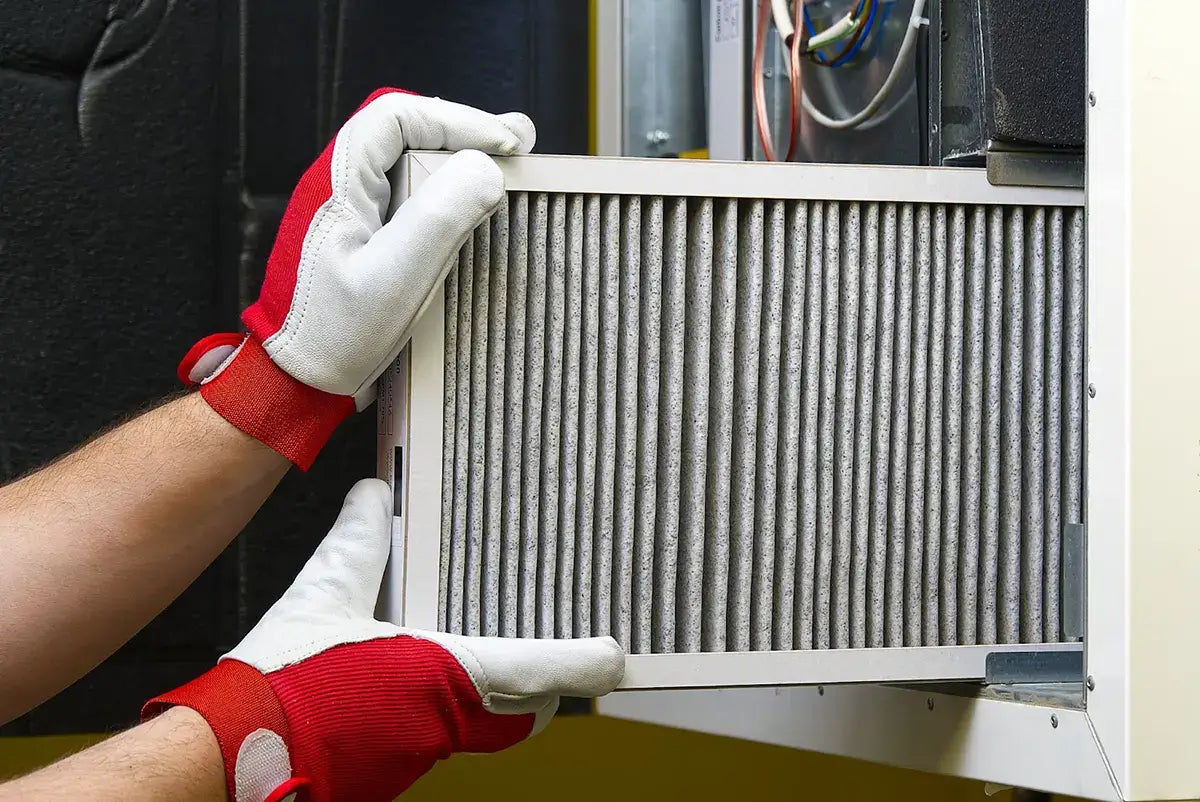 Technician performing air handler maintenance by replacing a filter in an HVAC system.