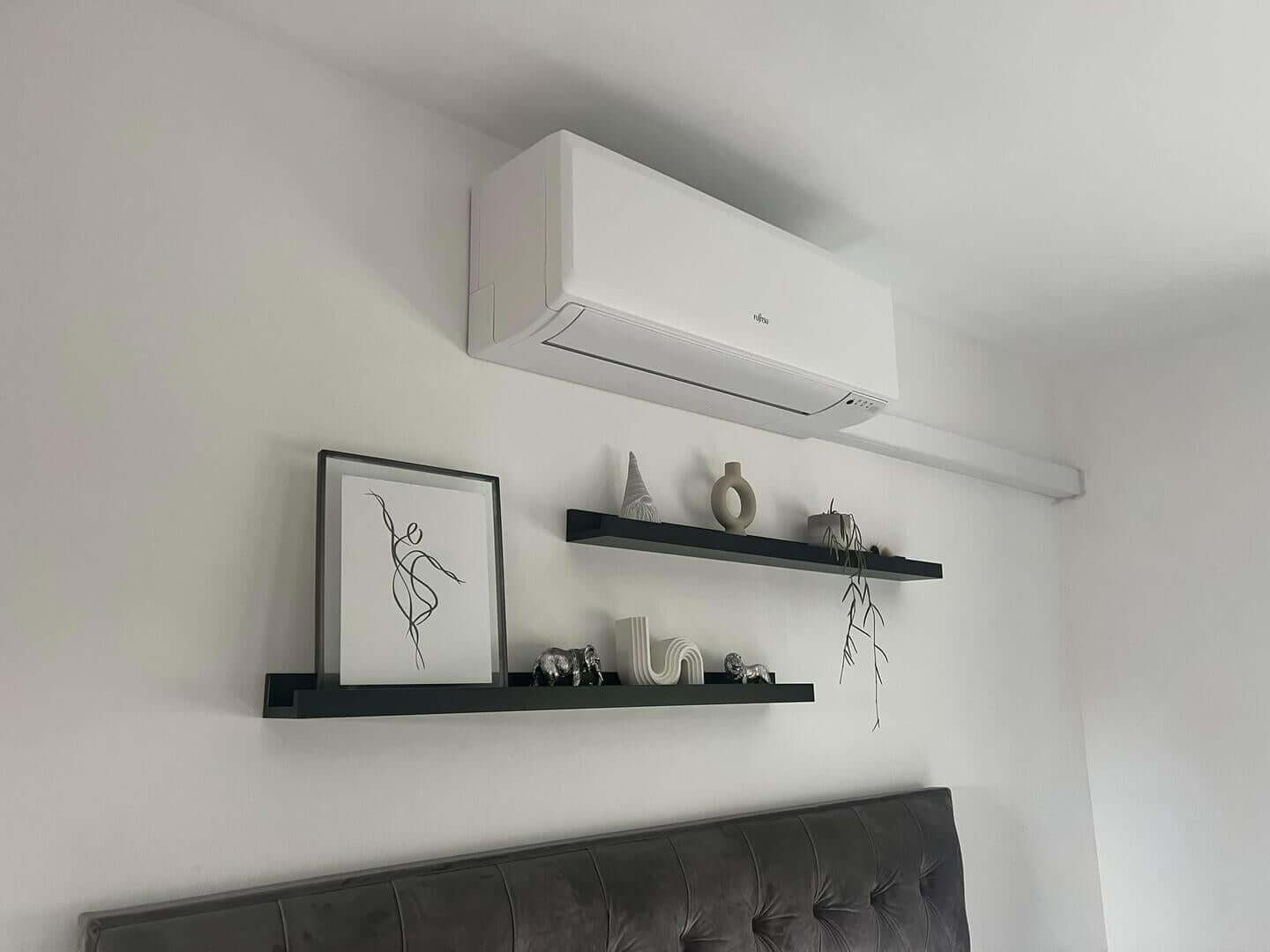 Stylish air conditioning installation in a modern domestic bedroom with shelves and decor.